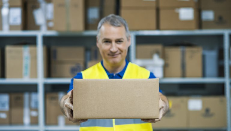 Smiling warehouse workers preparing a shipment in a large warehouse. Factory worker. Delivery check. Warehouse worker holding package.